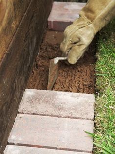 a person digging in the ground with a trowel next to brick wall and grass