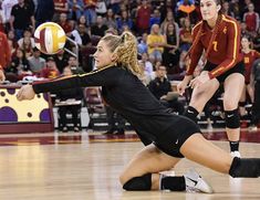 two women are playing volleyball in front of an audience at a sporting event, one is reaching for the ball