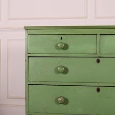 a green chest of drawers with knobs on the top and bottom, in front of a white wall