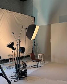 a photo studio with several lighting equipment and chairs in front of a white backdrop that is draped over