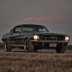 an old black car is parked in a field at dusk with the sun shining on it's headlight