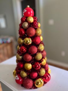 a red and gold christmas tree with ornaments on it's top sitting on a table