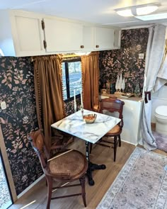 a dining room table and chairs in front of a window with floral wallpaper on the walls