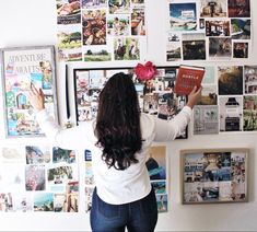 a woman standing in front of a wall with many pictures on it and reading a book