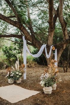 an outdoor ceremony setup with white draping, flowers and greenery on the ground