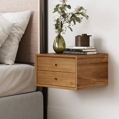 a nightstand with two drawers and a vase on it next to a bed in a bedroom