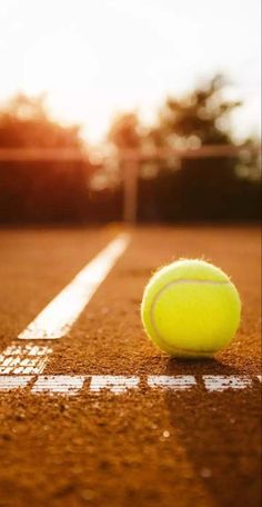 a tennis ball sitting on top of a tennis court with the sun in the background