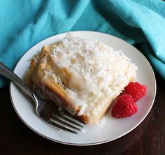 a white plate topped with a piece of cake and raspberries next to a fork