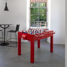 a red foosball table sitting in front of a window next to a bar stool