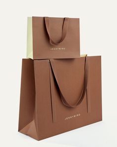 two brown shopping bags sitting side by side on a white surface with the handles down