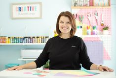 a woman sitting at a table with some crafting supplies on the wall behind her