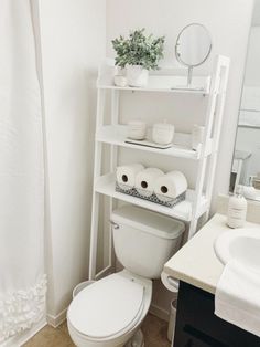 a white toilet sitting under a bathroom mirror next to a shelf filled with rolls of toilet paper