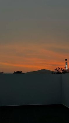 the sun is setting behind a building with a clock tower in the foreground and mountains in the distance