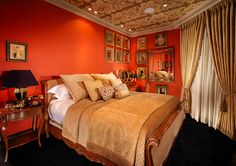 a bedroom with red walls and gold bedding in the center is decorated with pictures on the wall