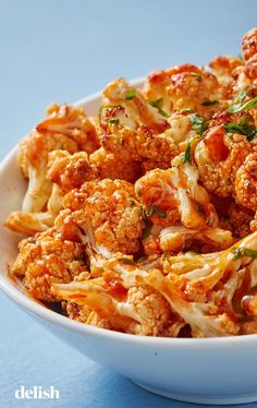 a white bowl filled with pasta covered in sauce and cheese, sitting on a blue surface