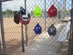 several baseball caps are hanging on the fence at a ball park, and there is no image here to provide a caption for