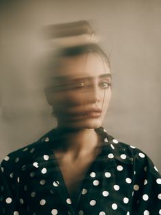 a woman is standing in front of a wall and she has her hair pulled back