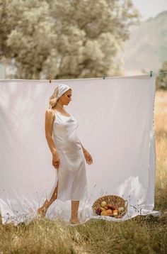 a woman in white dress standing next to a laundry line with apples on the ground