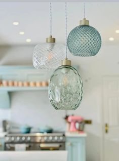 three glass globes hanging from the ceiling in a kitchen with blue cabinets and white countertops