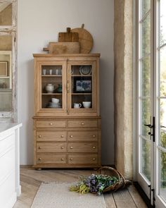 a wooden china cabinet sitting next to a window in a room with wood floors and white walls