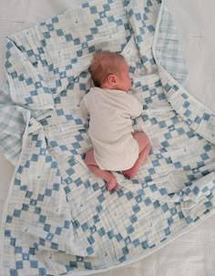 a baby wrapped up in a blanket on top of a bed with blue and white checkered sheets