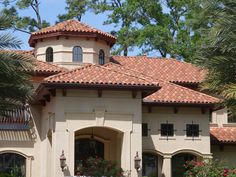 a large house with red tile roof and palm trees in the front yard on a sunny day