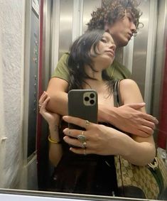 a woman taking a selfie in the mirror with her cell phone while standing next to a man