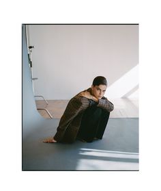 a woman sitting on the floor in front of a wall with her hand on her head