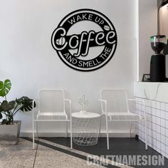 the coffee and smell sign is on the wall in front of two white chairs, with a potted plant next to it