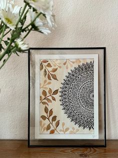 a vase filled with white flowers sitting next to a framed art print on top of a wooden table