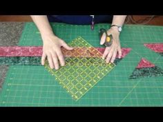 someone is cutting fabric with scissors on a green tablecloth that has red and yellow squares