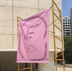 a pink banner is hanging on a scaffold in front of a building