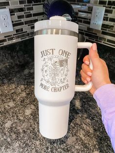 a person holding a white coffee cup on top of a counter