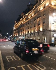 cars driving down the street at night in front of a large building with lights on