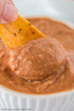 a hand dipping a tortilla chip into a bowl of salsa