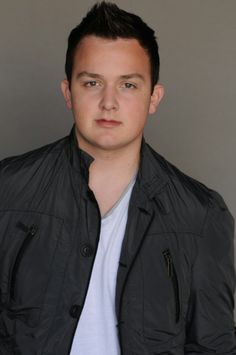 a young man in a black jacket and white t - shirt is looking at the camera