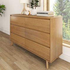 a wooden dresser sitting in front of a window next to a potted plant on top of a hard wood floor