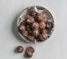 a bowl filled with chocolate covered donuts on top of a white countertop next to three pieces of paper