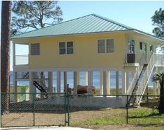 a yellow house sitting on top of a lush green field next to the ocean with stairs leading up to it