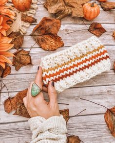 a woman's hand holding an orange and white crochet purse on top of leaves