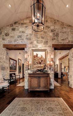 a living room with stone walls and wood floors, an area rug and chandelier hanging from the ceiling