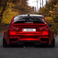 a red car parked on the side of a road in front of trees and leaves