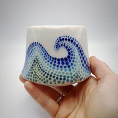 a hand holding a white and blue ceramic object with dots on it's surface