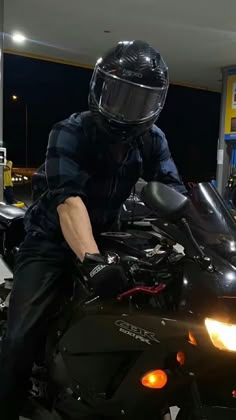 a man sitting on top of a motorcycle at a gas station with his helmet on