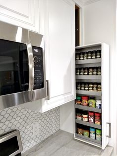 a kitchen with white cabinets and stainless steel microwave above the pantry shelve filled with food