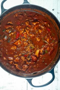 a large pot filled with lots of food on top of a wooden table next to a white wall