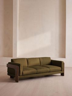 a green couch sitting on top of a hard wood floor next to a white wall