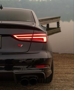 the rear end of a black car parked in front of a body of water with a dock