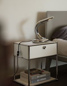 a nightstand with a lamp on top of it next to a bed and a book