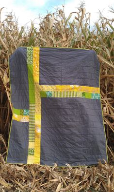 a black and yellow quilt sitting in the middle of a corn field on top of dry grass